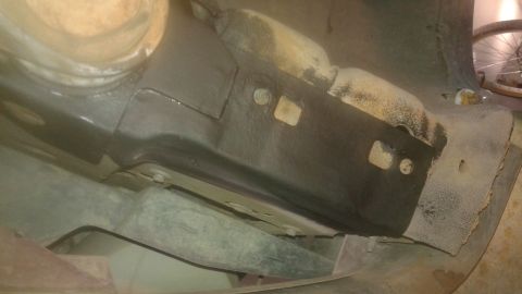 1996 Ford Bronco - Underside view of a vehicle's frame and suspension components, showing rust and some protective coating. A bicycle wheel is visible in the…