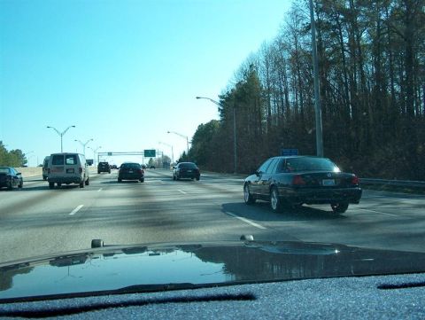 2001 Ford Crown Victoria - A black sedan is seen from behind on a highway with other vehicles.