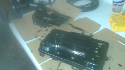 1996 Ford Bronco - Two black metal parts, possibly from a vehicle, are laid out on cardboard with black paint splattered around them. A yellow tool case and a…