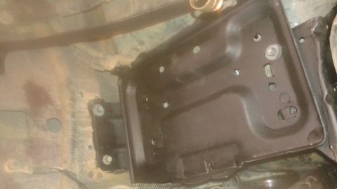 1996 Ford Bronco - A dark-colored metal battery tray is mounted to the underside of a vehicle. The tray has multiple circular openings and is secured with bol…