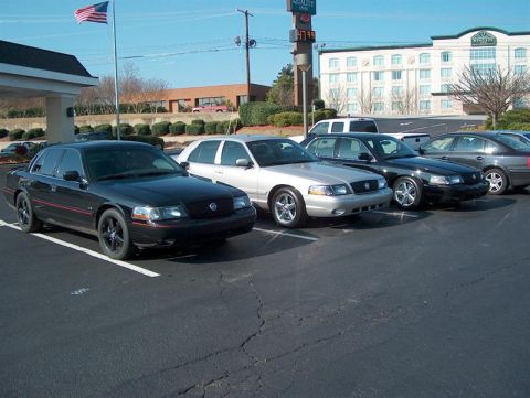 2001 Ford Crown Victoria - Several Ford Crown Victorias are parked in a lot, including a black model with red trim and custom wheels.