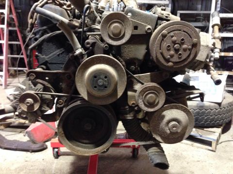 1979 Ford Bronco - A close-up, low-angle view of a heavily rusted engine assembly, likely from a 1979 Ford Bronco, mounted on a red engine stand. The engine f…
