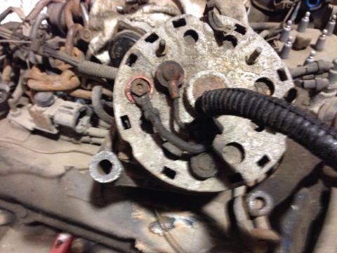1979 Ford Bronco - A close-up view of a dirty, metallic alternator with a black ribbed hose attached. The alternator is mounted on a vehicle's engine componen…