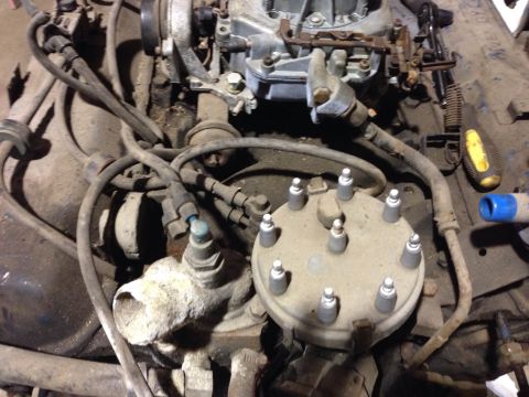 1979 Ford Bronco - A close-up view of a dusty engine bay, focusing on the distributor cap and carburetor. Various hoses and wiring are visible throughout the…
