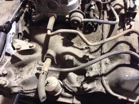 1979 Ford Bronco - A close-up, dusty view of an engine block with various hoses and metal lines attached. A ratchet is visible on the left side of the frame.