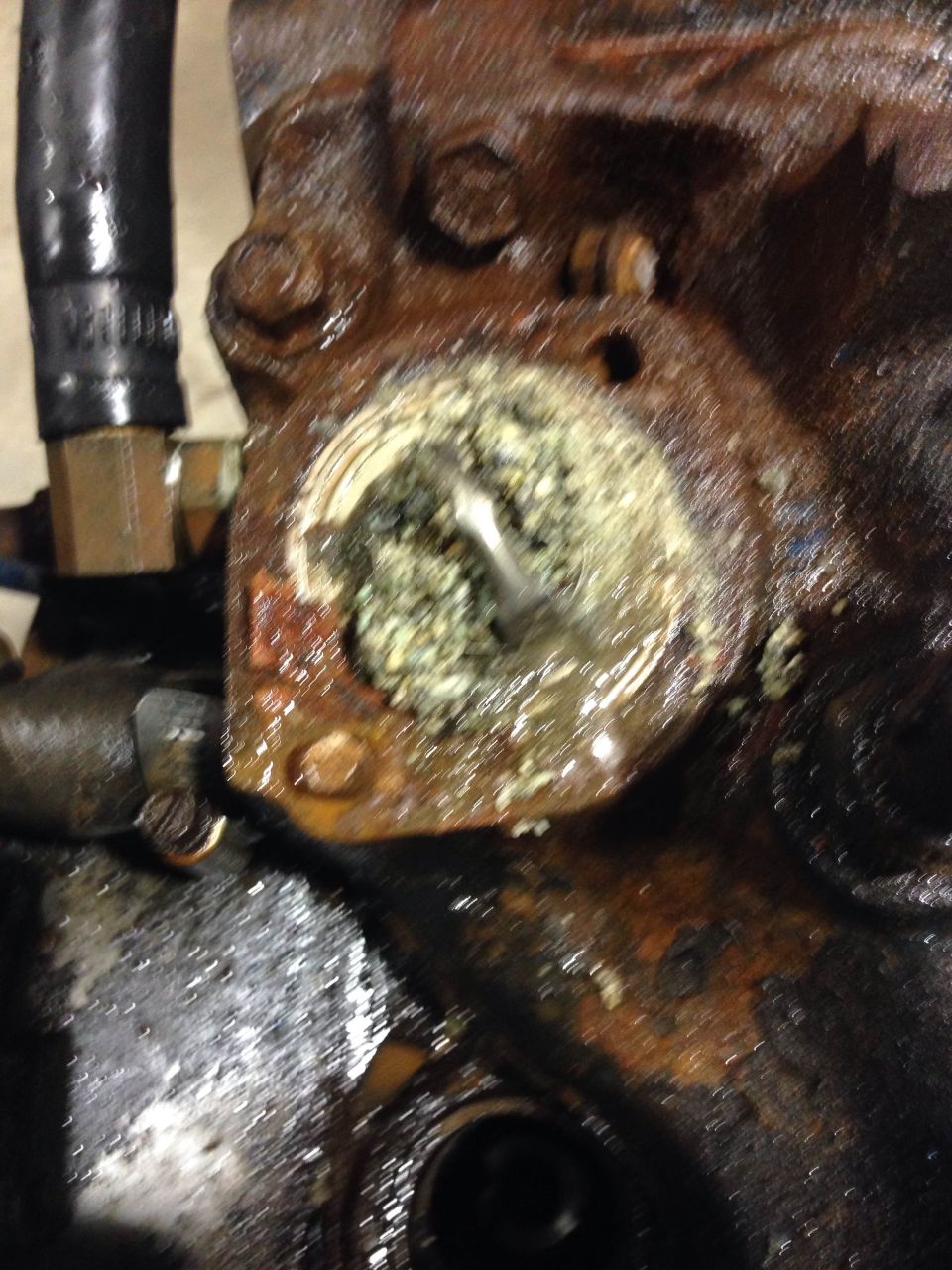 Heavily corroded engine part with green and white residue in a circular opening.
