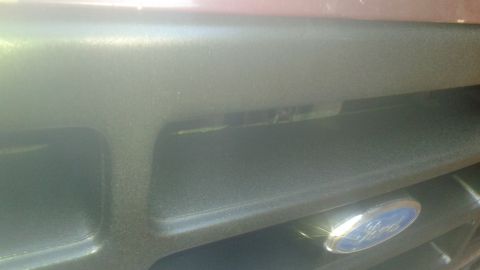 1996 Ford Bronco - A close-up view of the front grille of a vehicle, featuring a Ford emblem. The grille appears to be black plastic with horizontal bars.
