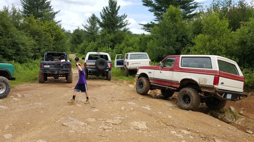 Off-road vehicles including Ford Broncos on a dirt trail with trees.