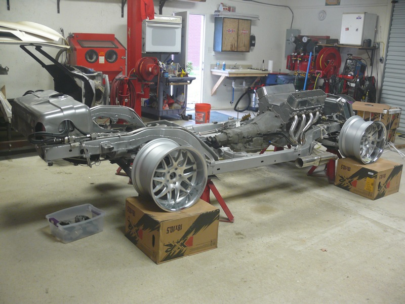 1976 Chevrolet Corvette chassis with V8 engine and transmission on jack stands in a garage.
