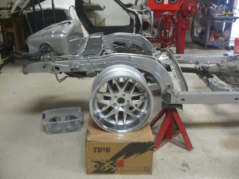 Silver car frame on jack stands with a large silver wheel on a box.