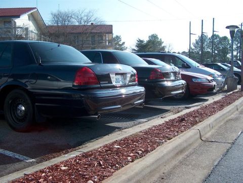 2001 Ford Crown Victoria - Several vehicles are parked in a lot on a sunny day. The closest vehicle is a black police car.