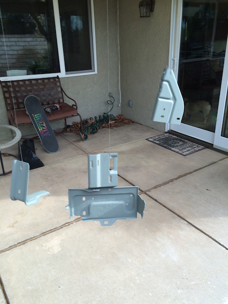 1981 Ford Bronco - Two painted metal parts are displayed on a concrete patio. One part is hanging from a string, and the other two are resting on the ground.
