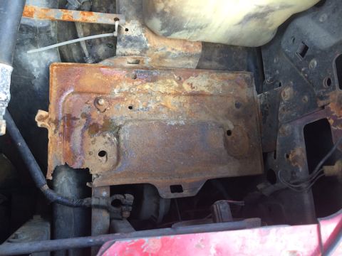 1981 Ford Bronco - A heavily rusted battery tray is visible in the engine bay of a vehicle. The tray is secured with a zip tie and shows significant corrosion…