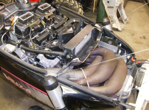 2000 Ford E350 - The engine compartment of a black Yamaha snowmobile is shown, featuring a complex exhaust system with multiple pipes and a visible radiator…