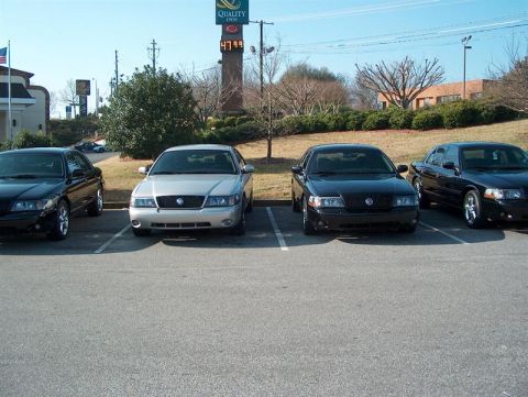 2001 Ford Crown Victoria - A silver Mercury Grand Marquis is parked alongside three black sedans in a parking lot.