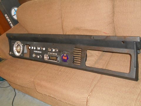 1972 Ford Bronco - A black dashboard panel with various gauges, switches, and a car stereo is displayed on a brown couch. The panel appears to be from an olde…