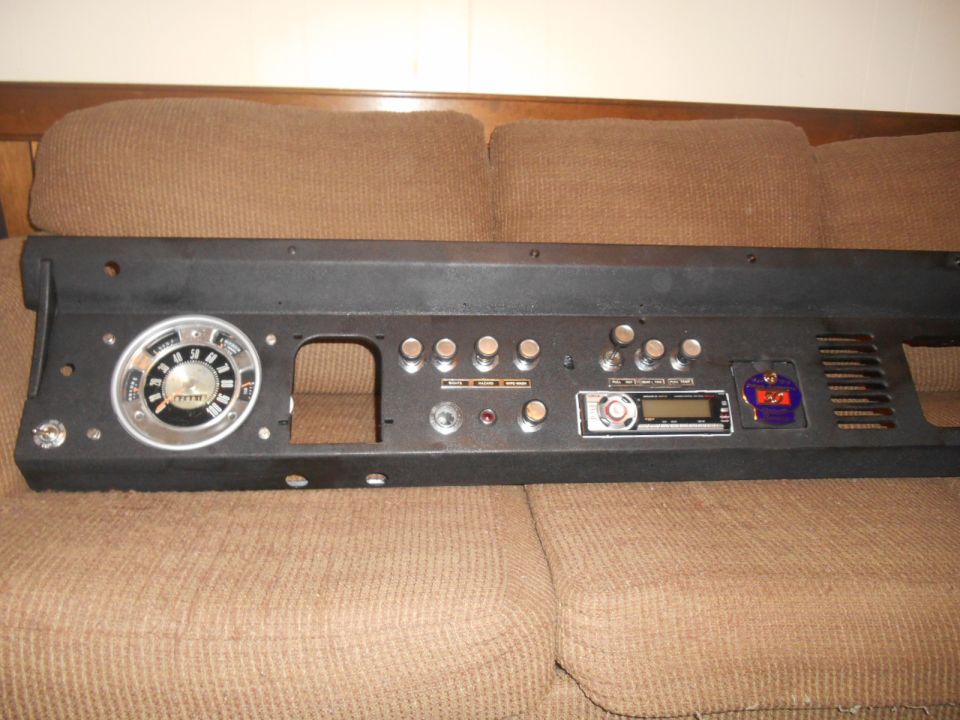 Black Ford Bronco dashboard panel with speedometer, radio, and emblem on a brown couch.