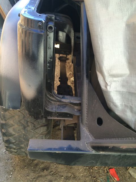 1987 Suzuki Samurai - Photo of the rear quarter panel, frame and bumper of a dark vehicle partly covered by a tarp.