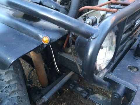 1987 Suzuki Samurai - Photo of the front of a Jeep showing a tubular brush guard, round headlight and amber turn signal.