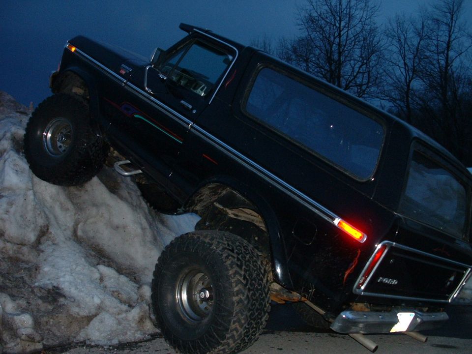 Black 1978 Ford Bronco climbing snow bank, 3/4 front view