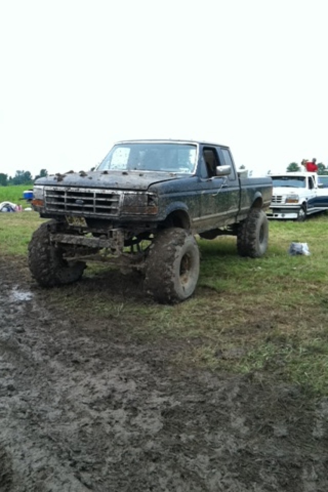 Muddy black 1995 Ford F-150 pickup truck with large tires in a field.