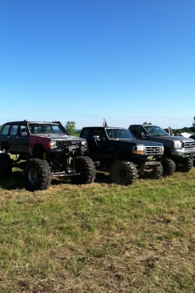 Three lifted off-road vehicles parked in a grassy field.