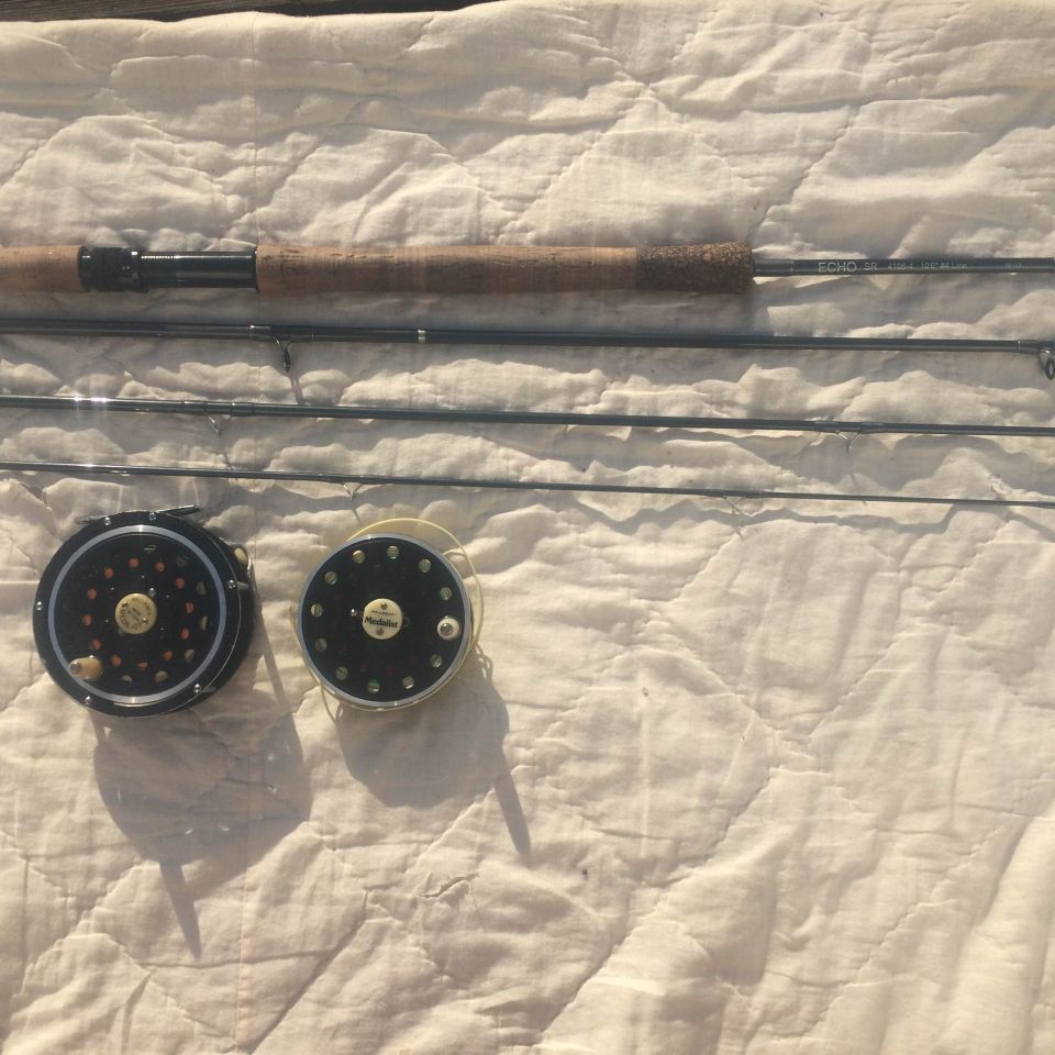 Fly fishing rod and two fly fishing reels on a quilted white surface.