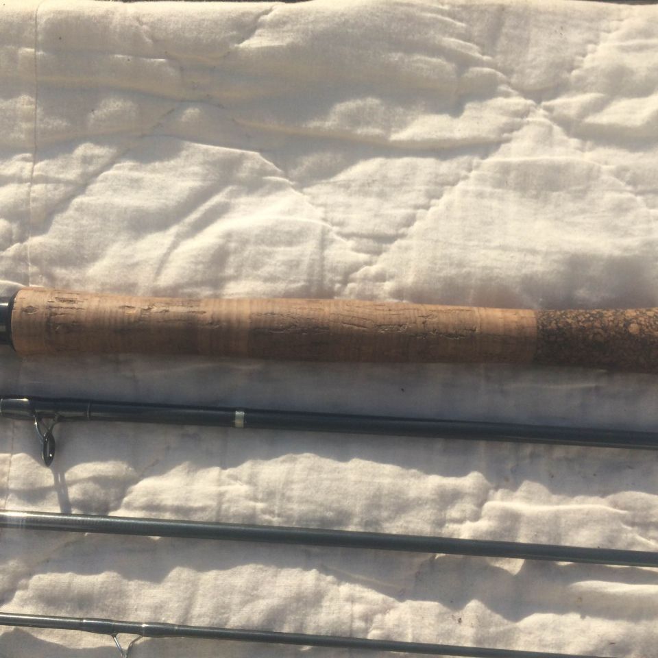 Fishing rod with cork handle on a white quilted surface.