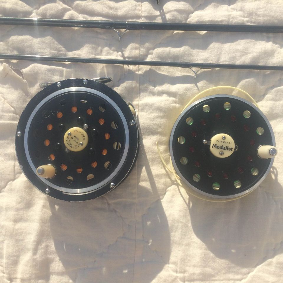 Two fishing reels and a fishing rod on a textured surface