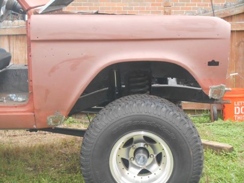 1972 Ford Bronco - Side view of a vintage Ford Bronco fender and wheel during a restoration. The vehicle is painted a reddish-brown primer and shows areas of…