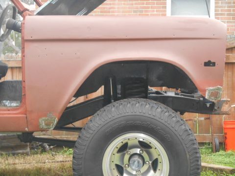 1972 Ford Bronco - Side view of a rusty orange 1972 Ford Bronco undergoing restoration. The vehicle's fender, wheel well, and tire are visible, along with par…