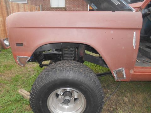 1972 Ford Bronco - The front fender and wheel of a red 1972 Ford Bronco project vehicle are shown. The fender has patches of bare metal and some holes, and th…