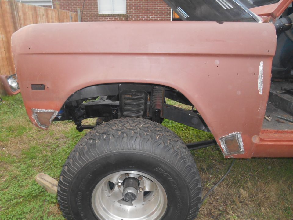 Red 1972 Ford Bronco front fender and wheel with visible suspension and bodywork patches.