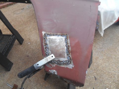 1972 Ford Bronco - A patch has been welded into a section of a rusty red vehicle panel. A welding clamp is attached to the edge of the panel.