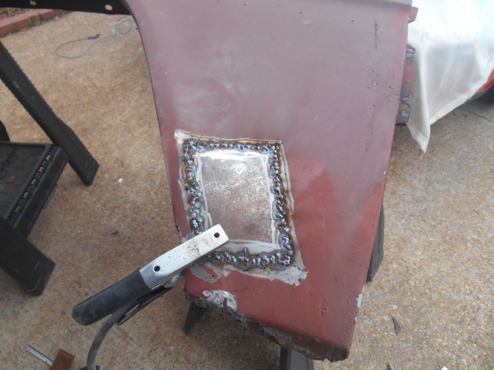 Welding patch on rusty red vehicle panel with clamp attached