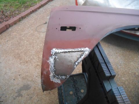 1972 Ford Bronco - A close-up view of a rusty red car fender with a patch of metal that has been welded and ground down. The fender is supported by a green sa…