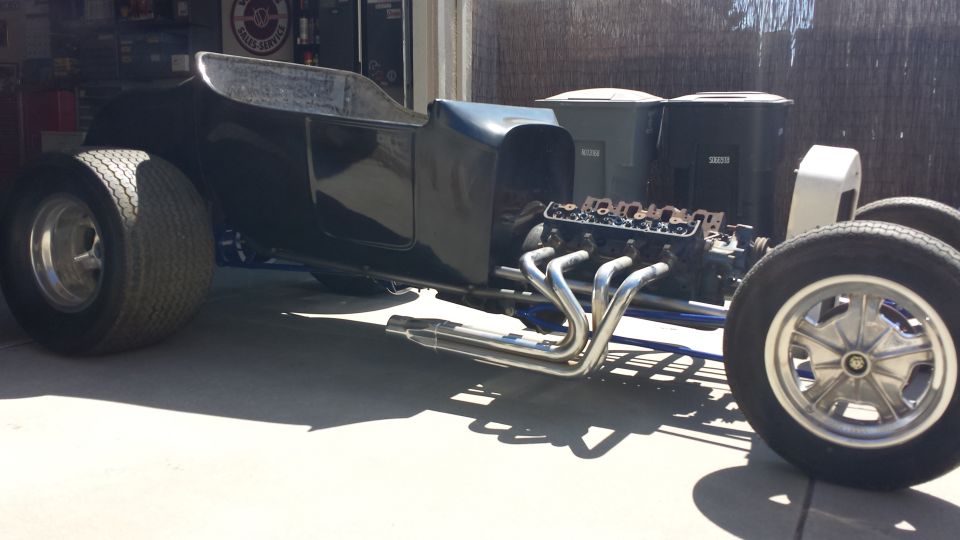 Black hot rod T-bucket with V8 engine and chrome headers, side view.
