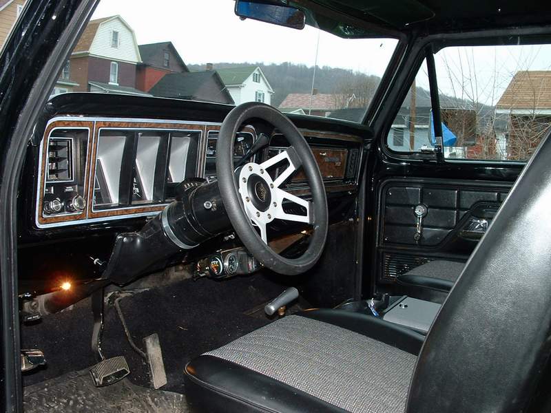 Interior of an older pickup with woodgrain dash, three-spoke wheel, gray cloth bench seat