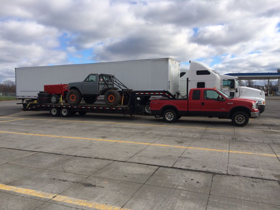 Red Ford F-250 pickup truck towing a trailer with a custom off-road vehicle.