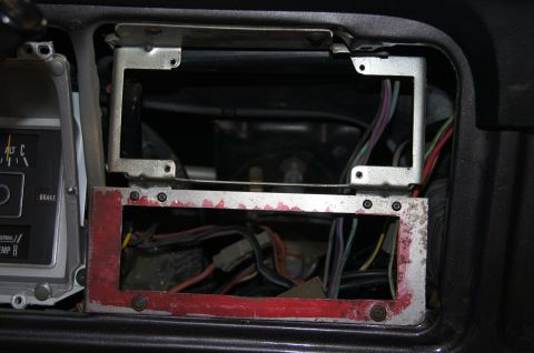 1979 Ford Bronco - A close-up view of a car's dashboard showing an open radio or accessory slot with exposed wiring. The slot has a metal bracket and a red-pa…
