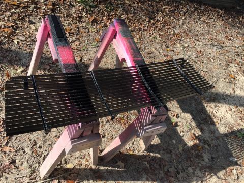 1996 Ford Bronco - A black metal grill is being spray painted black and pink while resting on two sawhorses outdoors.