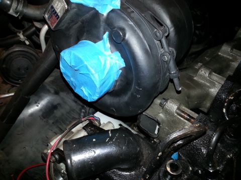 1994 Ford Bronco - A close-up view of a black engine component, possibly a turbocharger housing, with blue painter's tape covering a section of it. Metal brac…
