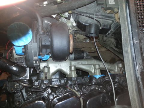 1994 Ford Bronco - A close-up view of a turbocharger installed on a black engine block, likely in a 1994 Ford Bronco. Blue tape is visible on parts of the tur…