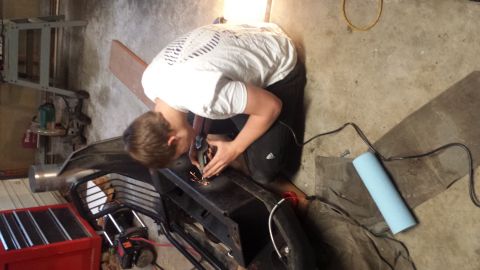 1996 Ford Bronco - A person is using a grinder on a black metal bumper or frame, with sparks flying. The scene appears to be a garage or workshop with tools a…