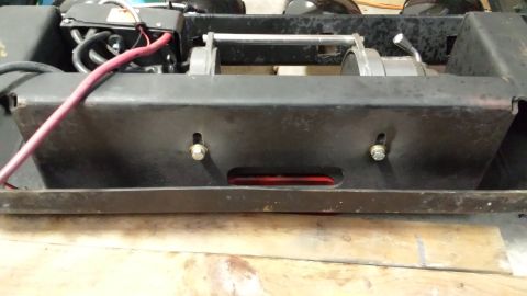 1996 Ford Bronco - A close-up view of a winch mounted on a black metal bracket, possibly part of a vehicle's front end. A thick red cable runs from the upper…