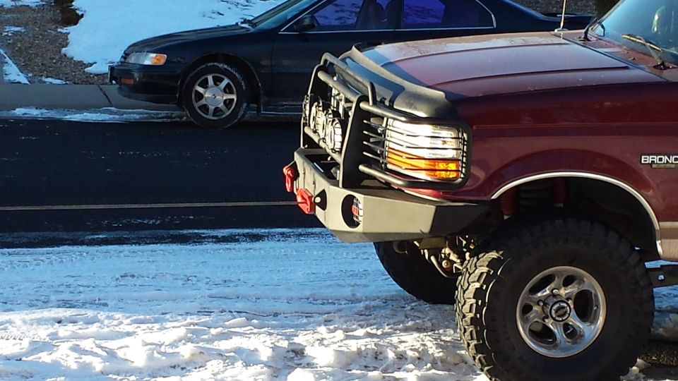 Front of a red Ford Bronco with custom bumper and grille guard, parked in snow.