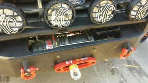1996 Ford Bronco - A close-up view of the front bumper of a Ford Bronco, featuring a winch, KC lights, and red recovery hooks.