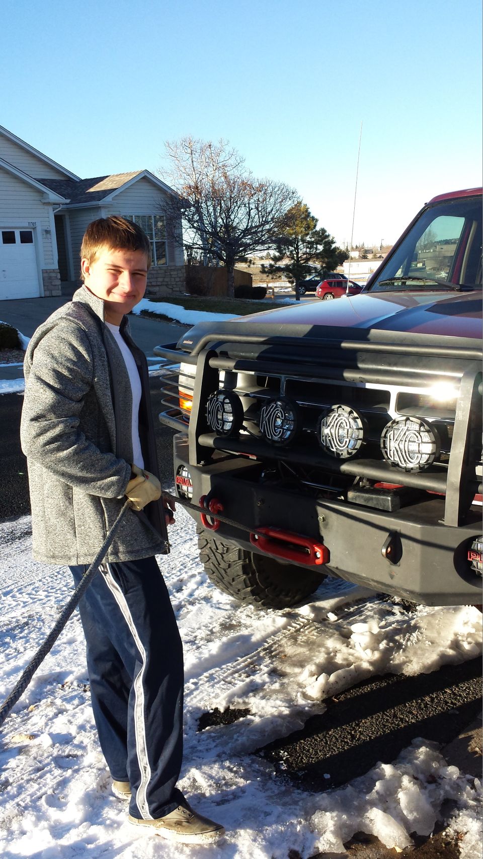 Young man holding tow rope next to a red SUV with KC lights and aftermarket bumper.
