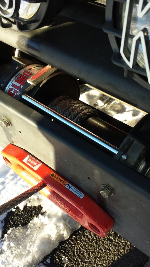 1996 Ford Bronco - A close-up view of a WARN M15 electric winch with a red shackle attached to the winch line. The winch is mounted on a vehicle's frame, with…