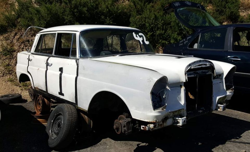 White vintage sedan with racing numbers '1' and '42', missing wheels and front end.